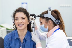 Hearing exam otolaryngologist doctor checking woman's ear using otoscope or auriscope at medical clinic