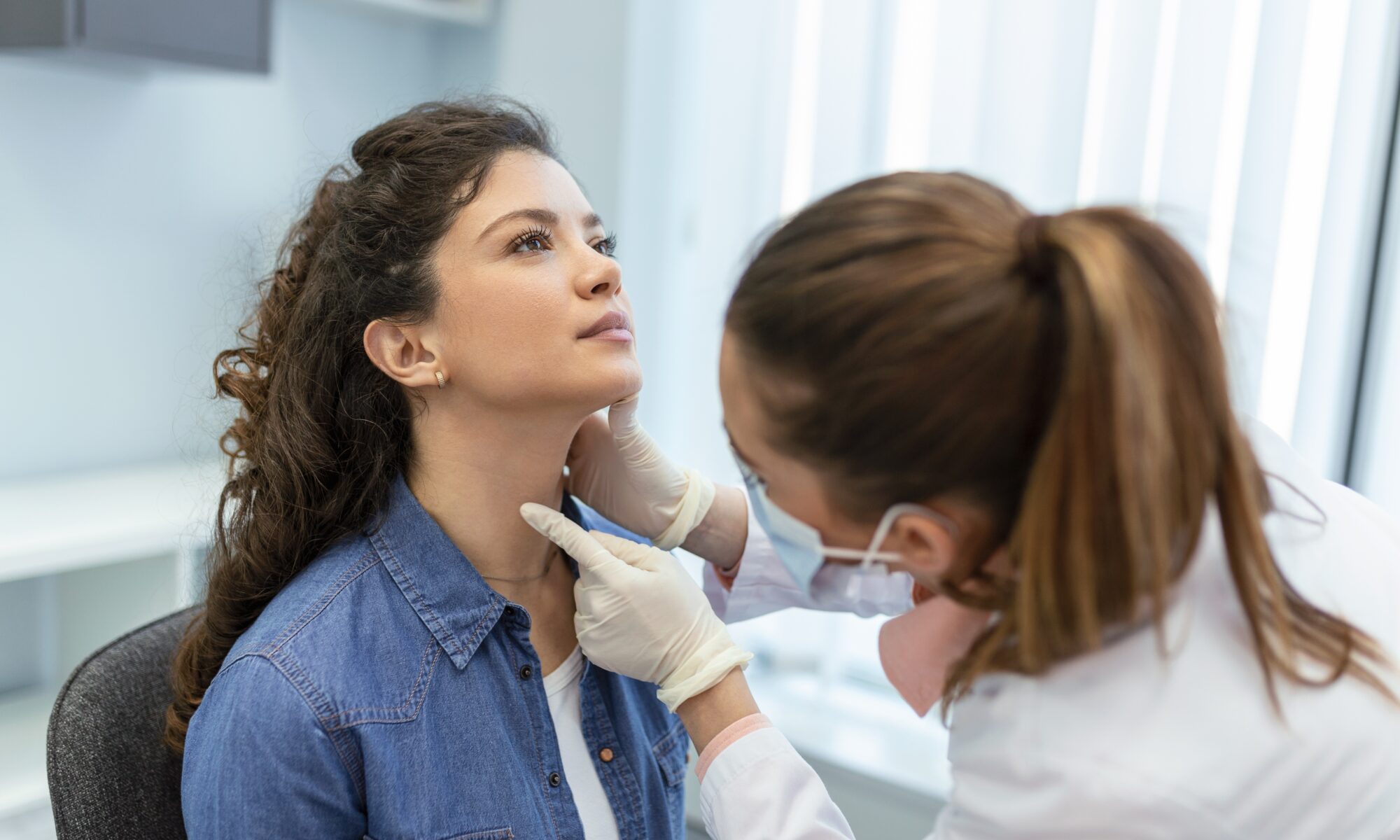 The best primary care doctors Orange, CT is depicted by a photo of a woman in a lab coat and mask examining the throat of a seated woman