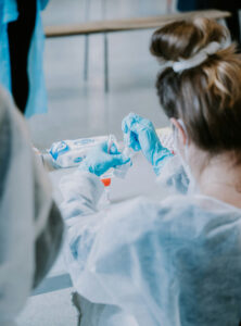 COVID testing in CT, depicted by a photo of a doctor holding a thermometer in one gloved hand and the chin of her seated patient in the other